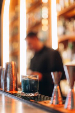 Sofistike bir kokteyl, bar teçhizatı ve ışıklandırmasının bulanık arka plan detaylarıyla bir barın üzerinde durur..