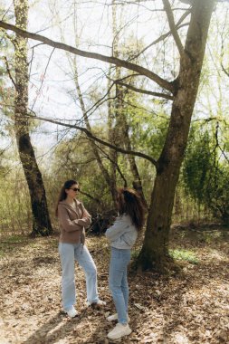İki birey birbirine dönük duruyor, sakin, ormanlık bir alanda düşünceli bir sohbete dalıyorlar, yumuşak doğal aydınlatma ve yemyeşil ışıklarla çevrili, bağlantı kurma ve tefekküre dalmayı çağrıştırıyor..