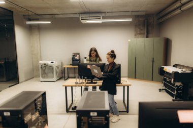 Masaüstü ve dizüstü bilgisayarlarda işbirliği yapan iki kişinin yer aldığı bir çalışma alanı. Çağdaş ofis, işbirlikçi bir çalışma ortamı sergileyen yazıcılar ve fotokopi makineleri de dahil olmak üzere gelişmiş ekipmanlar içerir..