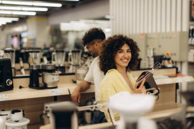 Perakende elektronik mağazasını keşfeden müşteriler, modern mutfak aletlerini ve aletlerini inceleyerek, alışveriş, tüketim ve yaşam tarzı seçimlerini temsil ediyorlar. Gülümseyen etkileşimler kararlarında neşeyi, memnuniyeti ve teknolojiyi yansıtıyor..