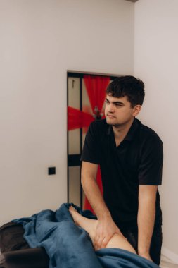 Yetenekli bir erkek masör huzurlu bir ortamda bir müşteriye terapatik bacak masajı sağlar. Kurulum, oturumda uzmanlık ve rahatlığın vurgulanması ve gevşemeyi teşvik ediyor..