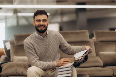 Çağdaş bir mobilya galerisinde kumaş seçeneklerini araştıran neşeli bir adam, dostane bir tavırla döşeme seçimleri sergiliyor..