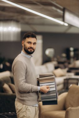 Zarif bir mobilya mağazasında kumaş örnekleri seçen şık bir birey. Gelişmiş tasarım ve detaylara dikkat, çağdaş iç moda eğilimlerini vurguluyor.