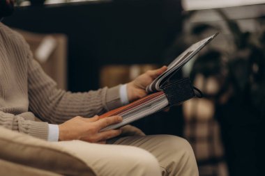 Bir adam rahat bir şekilde oturur, kitap okumaya dalmış, evde dingin ve odaklanmış bir atmosfer yaratır..