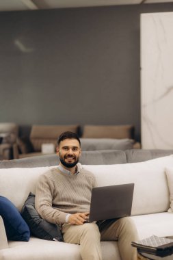 Rahat bir koltuğa oturmuş, modern ve şık bir ortamda dizüstü bilgisayar kullanan kendine güvenen bir birey. Çevre, verimlilik, konfor ve iş ve eğlence faaliyetleri için uygun çağdaş bir estetik sunar..