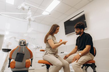 Modern diş sağlığı kliniğinde diş modelini kullanarak hastaya diş tedavisini açıklayan kadın dişçi.