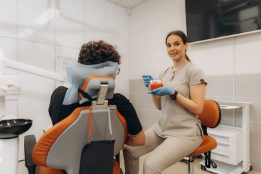 Modern diş kliniğinde bir diş modelini kullanarak hastaya diş tedavisini açıklayan kadın diş hekimi.
