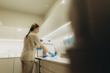 Mavi eldiven giyen hemşire otoklavın içindeki hastane veya klinik laboratuvarında tıbbi aletleri sterilize ediyor.