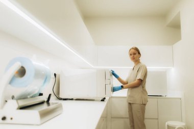 Eldiven giyen hemşire, parlak ve modern bir klinikte, temiz ve güvenli bir ortam sağlamak için gelişmiş sterilizasyon ekipmanları kullanıyor.
