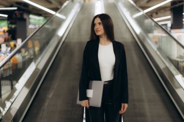 Kendine güvenen profesyonel, bir dizüstü bilgisayar tutuyor. Kapalı bir merdivende seyahat ederken, çağdaş bir ortamda dengeli bir tavır sergiliyor, kariyer odaklı odaklanma ve şık bir stil sergiliyor..