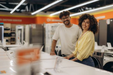 Neşeli çift elektronik mağazasında aletleri karıştırıyor ve inceliyor, alışveriş deneyimlerinin tadını çıkarıyorlar..