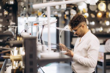 Bir adam modern aydınlatma aletini ev eşyaları ve dekorasyonlar için şık bir mağazada dikkatlice inceliyor. Ayar, çağdaş iç tasarım seçeneklerini ve optimal ışıklandırma sürecini vurgular.