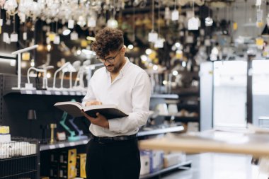 Lamba vitrinleriyle çevrili modern bir aydınlatma galerisinde alışveriş yapan bir adam..