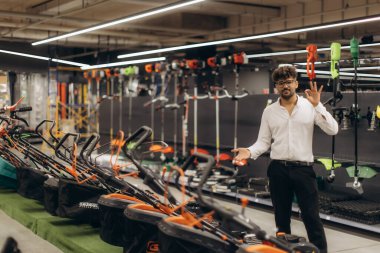 Bir mağazadaki profesyonel bir adam çeşitli yüksek kaliteli bahçe aletleri ve makineler sergileyerek müşteri odaklı hizmet sunar. Şehir merkezi, modern bahçe malzemelerinin sergilendiği organize bir yer..