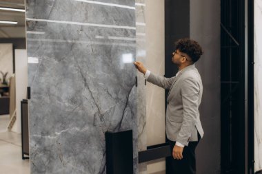 Takım elbiseli profesyonel bir adam büyük bir dekoratif taş paneli inceliyor, muhtemelen bir tasarım projesi ya da mimari seçilim için. Dekorun modern ve zarif bir atmosferi var..