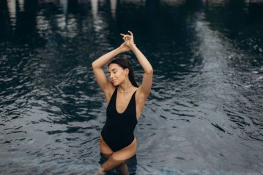 Yüzme havuzunda dinlenen bir turist, gözleri kapalı ve kolları havada, yaz güneşinin tadını çıkarırken lüks bir tatilin tadını çıkarıyor.