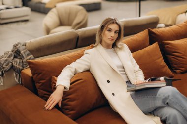 Zarif bir kadın şık bir oturma odasındaki koltukta rahat bir şekilde oturur, elinde bir dergi, modern iç tasarım ve rahatlık ve sofistike bir yaşam tarzı sergiler..