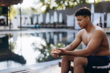 Genç erkek yüzücü, yaz aylarında havuz başında aldığı eğitimde cilt korumasına öncelik vererek ellerine dikkatlice güneş kremi sürüyor.