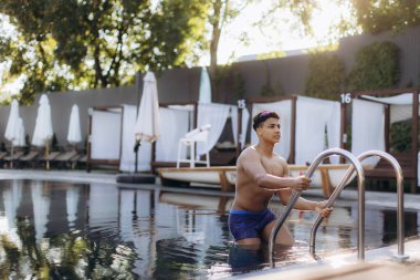 Genç sporcu yazın lüks bir tatil köyünde metal merdiven kullanarak havuzdan çıkıyor.