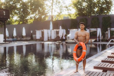 Cankurtaran havuz başında can simidi tutuyor, güneşli bir günde lüks bir otel havuzunda güvenliği sağlıyor.