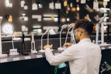 Modern bir mağazada lambaları inceleyen bir adam aydınlatma seçeneklerini parlak bir ambientte seçer..