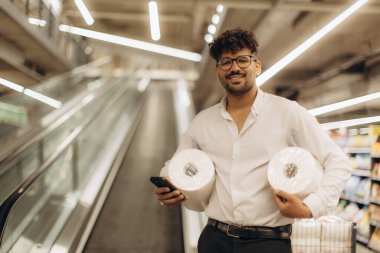 Bir adam mağazada mutlu bir şekilde poz verir ve neşeli bir alışveriş ortamı sunar..