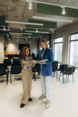 Modern mobilyalarla parlak ve çağdaş ofis ortamında dokümanları tartışan iki profesyonel kadın, takım çalışması ve iş birliği için üretken bir atmosfer yaratıyor..