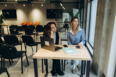 Geniş bir ofis ortamında masa başı iş birliği yapan iki profesyonel kadın, takım çalışması, üretkenlik ve modern çalışma alanı tasarımını örnek göstermektedir..