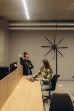Çağdaş bir ofis ortamında uzun bir masada iletişim kuran iki iş arkadaşı..
