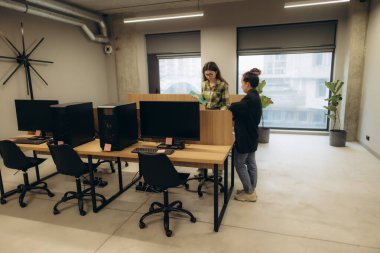 Bilgisayarları, bitkileri ve parlak atmosferi olan masaları olan modern bir ofis. İki meslektaş, çağdaş bir ortamda takım çalışması ve üretkenliği vurgulayarak profesyonel ve şık bir çalışma alanında işbirliği yapmaktadır..