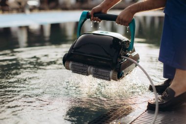 Havuz temizleyicisi otomatik bir robot temizleyicisi tutuyor, yazın köpüklü bir yüzme havuzunu verimli bir şekilde sürdürmeye hazırlanıyor.