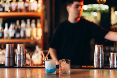 Bir barmen, yüksek kaliteli karıştırma araçları ve zarif kokteyllere odaklanarak canlı bir bar ortamında içki hazırlar. Çevre, miksoloji üzerine odaklanmış canlı bir sosyal ortamı yansıtır..