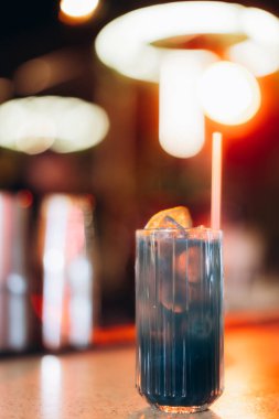 Bardakta turuncu bir garnitürle renkli bir kokteyl, parlak bir ışık saçarak, şık ve keyifli bir gece atmosferi yaratıyor..
