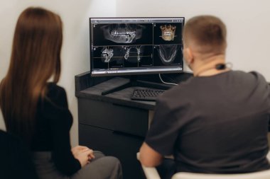 Modern diş hekimi, dişçi ve hasta ekrandaki detaylı oral görüntüleme taramalarını inceliyor..
