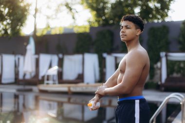 Genç adam koluna güneş kremi sürüyor, güneşli bir günde havuz kenarında güneşlenirken güneş yanığına karşı önlem alıyor.