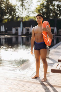 Havuzun kenarında duran genç cankurtaran, can simidi tutuyor, güvenliği sağlıyor ve yüzücülere yardım etmeye hazır.