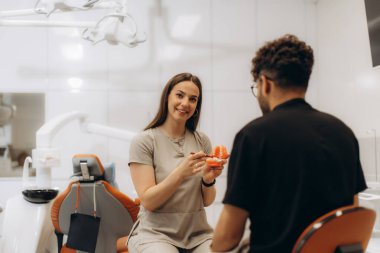 Diş sağlığı kliniğinde anatomik model kullanan hastaya doğru diş fırçalama tekniğini açıklayan dişçi.