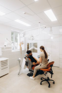 Modern klinikte erkek hastayı diş tedavisine hazırlayan dişçi, oral sağlık ve profesyonel bakıma odaklanıyor.