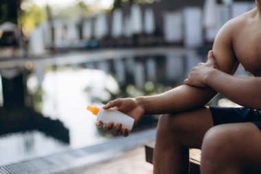 Güneş kremi tutan yüzücü, yaz aylarında yüzmek için ferahlatıcı havuz suyuna dalmadan önce güneş kremi sürmeye hazırlanıyor.