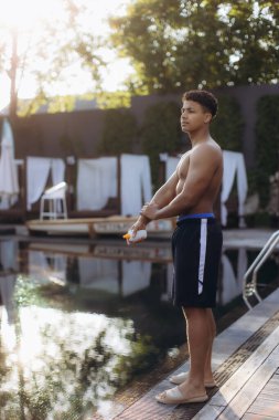 Genç adam koluna özenle güneş kremi sürüyor, havuz başında dinlendirici bir günün keyfini çıkarırken önceliği güneş güvenliğine veriyor.