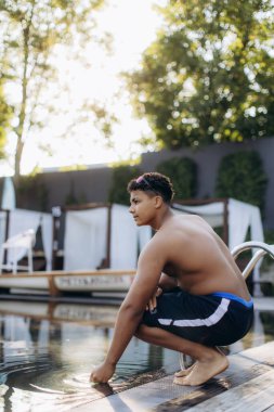 Genç yüzücü eğitime başlamadan önce havuz suyunu kontrol ediyor, yaz tatilinin keyfini çıkarıyor.