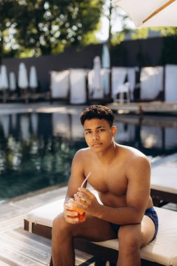 Turistin yüzme havuzunun yanında ferahlatıcı bir içeceğin tadını çıkarması, dinlendirici bir tatil sırasında lüks bir tatil yerinde yaz güneşinin tadını çıkarması.
