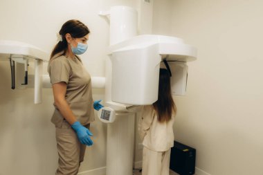 Diş hekimi panoramik bir diş röntgeni makinesi kullanıyor. Genç bir hastanın dişlerinin ve çenesinin detaylı bir resmini çekiyor.