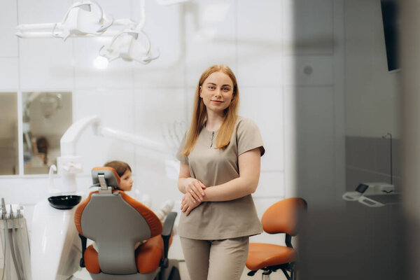 Female dentist standing in her office while a child patient sits in the dental chair, waiting for treatment