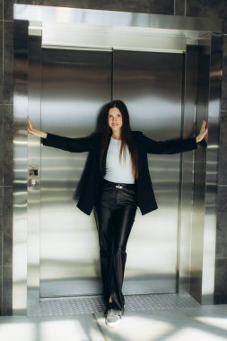 Profesyonel bir kadın modaya uygun giyinmiş bir asansöre yaslanır. Modern bir ortamda kararlılık ve tarz gösterir..
