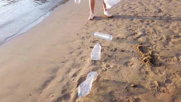 海滩上擦塑料的女人志愿者用垃圾袋收集垃圾 对海洋的塑料污染 可持续性概念 自愿清除塑料和清洁地球上的自然 — 图库视频影像