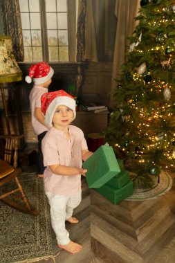 Çocuklar Noel 'i kutluyor, Noel Baba şapkalı iki çocuk hediye kutularını yerleştiriyor ya da açıyor.