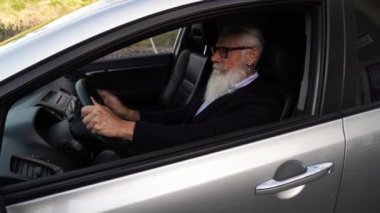 Arabada kıdemli bir adam arama yapıyor ve yeşil ekranlı telefonu gösteriyor.