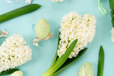 Beyaz bahar çiçekleri ve renkli yumurtaların olduğu Paskalya sahnesi mavi arka planda yatıyordu.