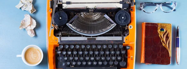 橙色的老式打字机 咖啡和笔记本在蓝色背景上的工作区 — 图库照片